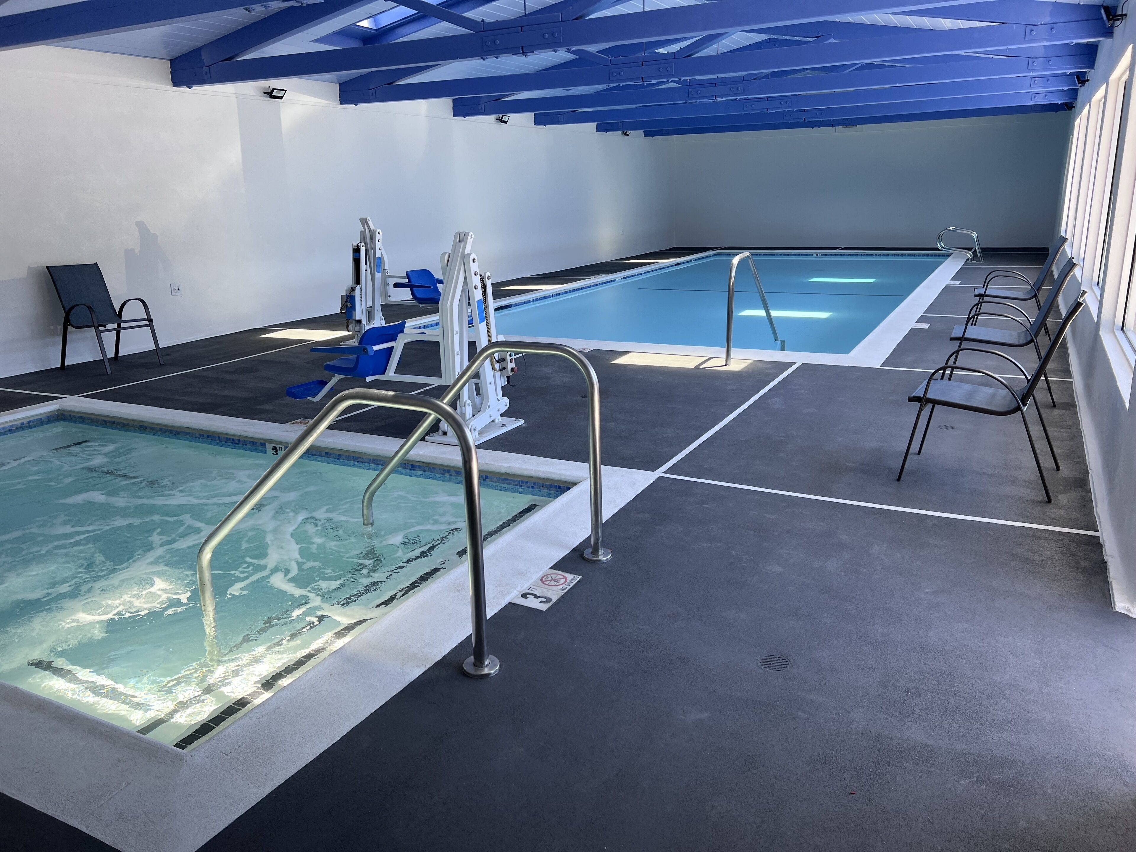 An indoor swimming pool with clear water, blue chairs, and a blue ceiling structure.