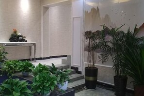 A lobby with a reception desk, a staircase, and potted plants.