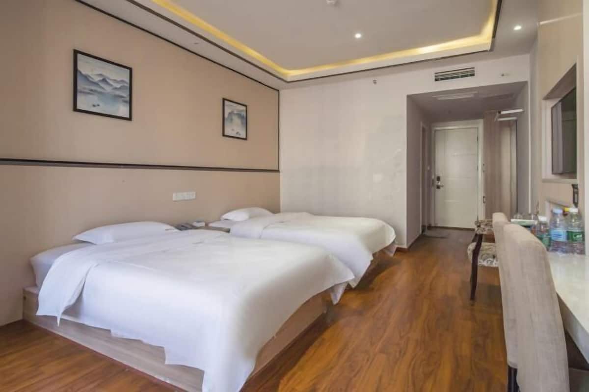 Habitación de hotel con dos camas, piso de madera, baño con espejo y una pequeña mesa con artículos de aseo.