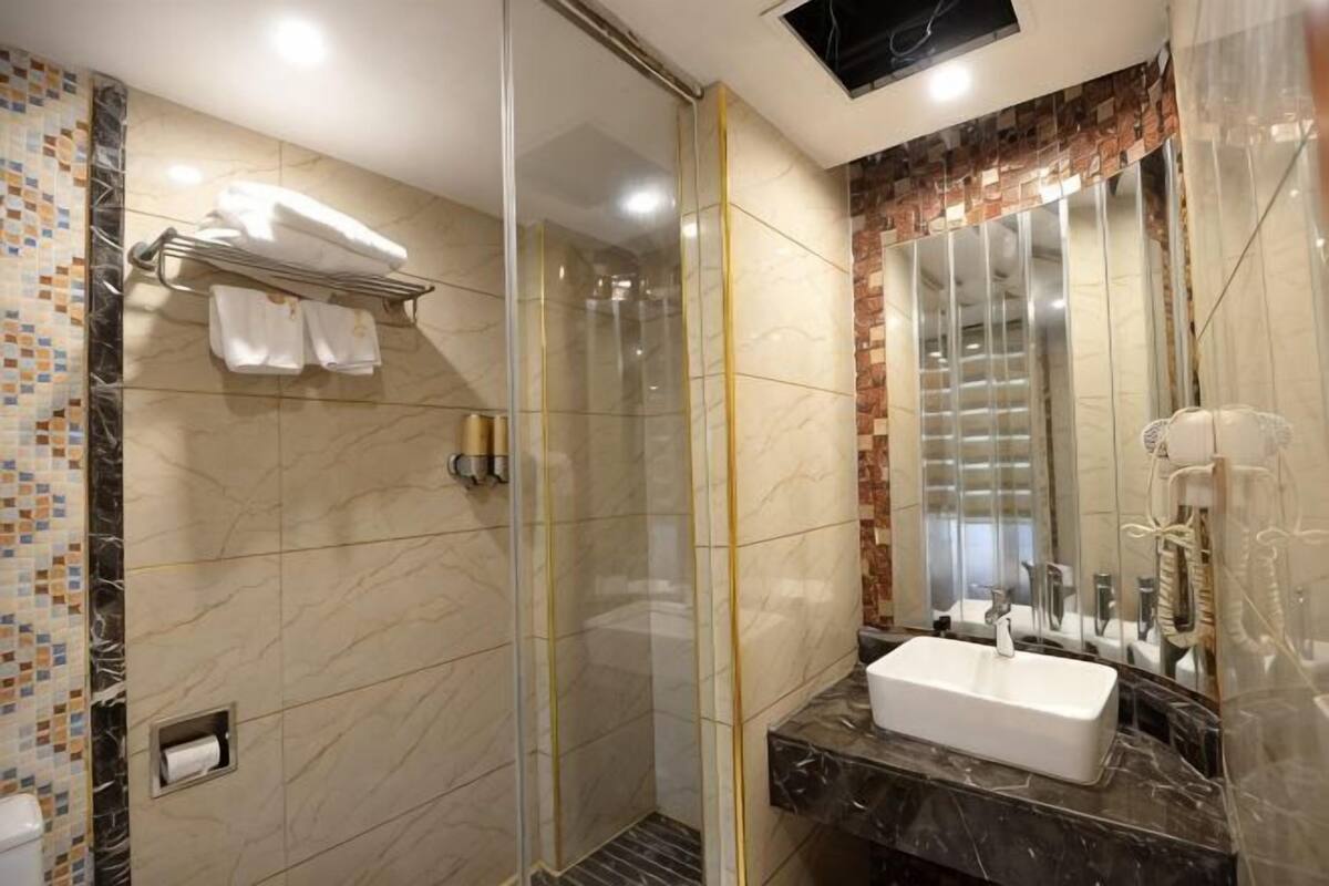 Un baño moderno con ducha de vidrio, lavamanos de mármol y un espejo grande.