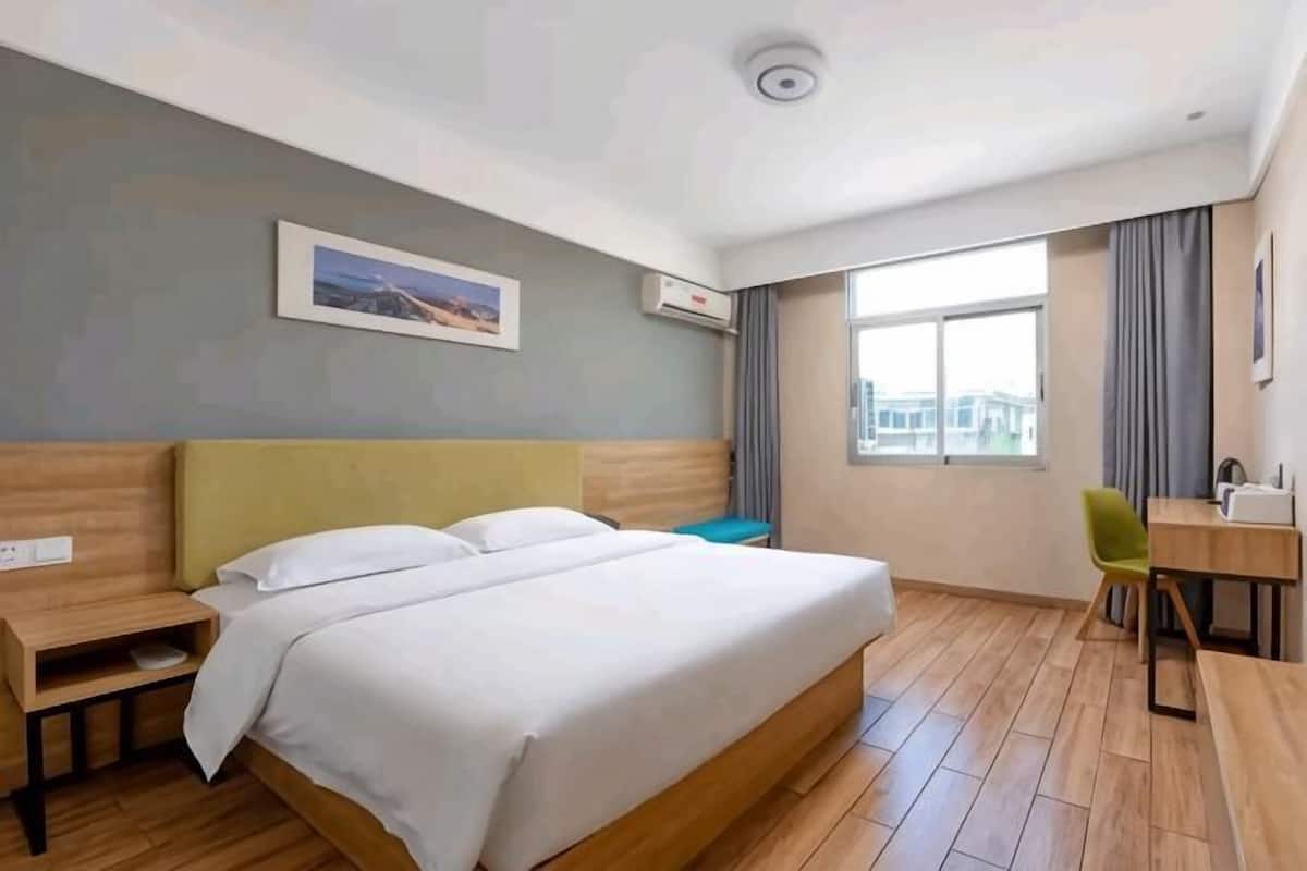 Una habitación de hotel con cama, escritorio, silla, ventana y un cuadro en la pared.