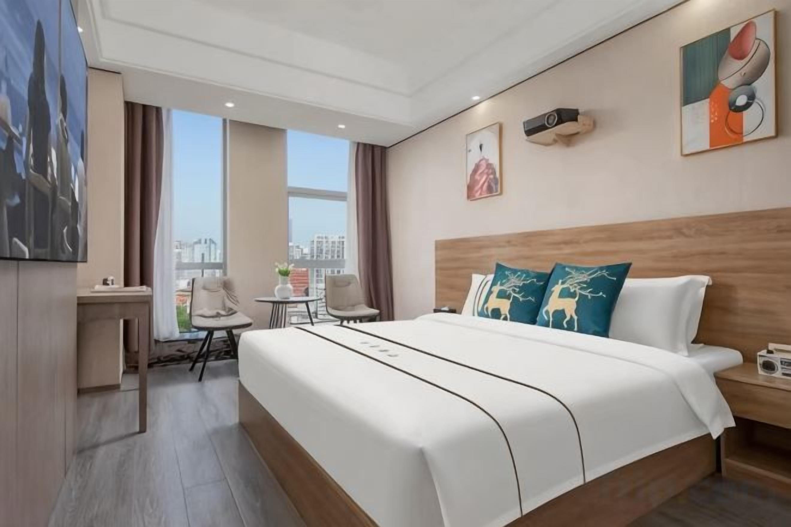 A hotel room with a large bed, a desk, a chair, and a view of the city.