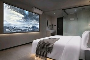A modern hotel room with a large bed, a bedside table, a mirror, and a large wall-mounted TV displaying a scenic image. - Yuedu Yizhan Fashion Hotel (Yichun)