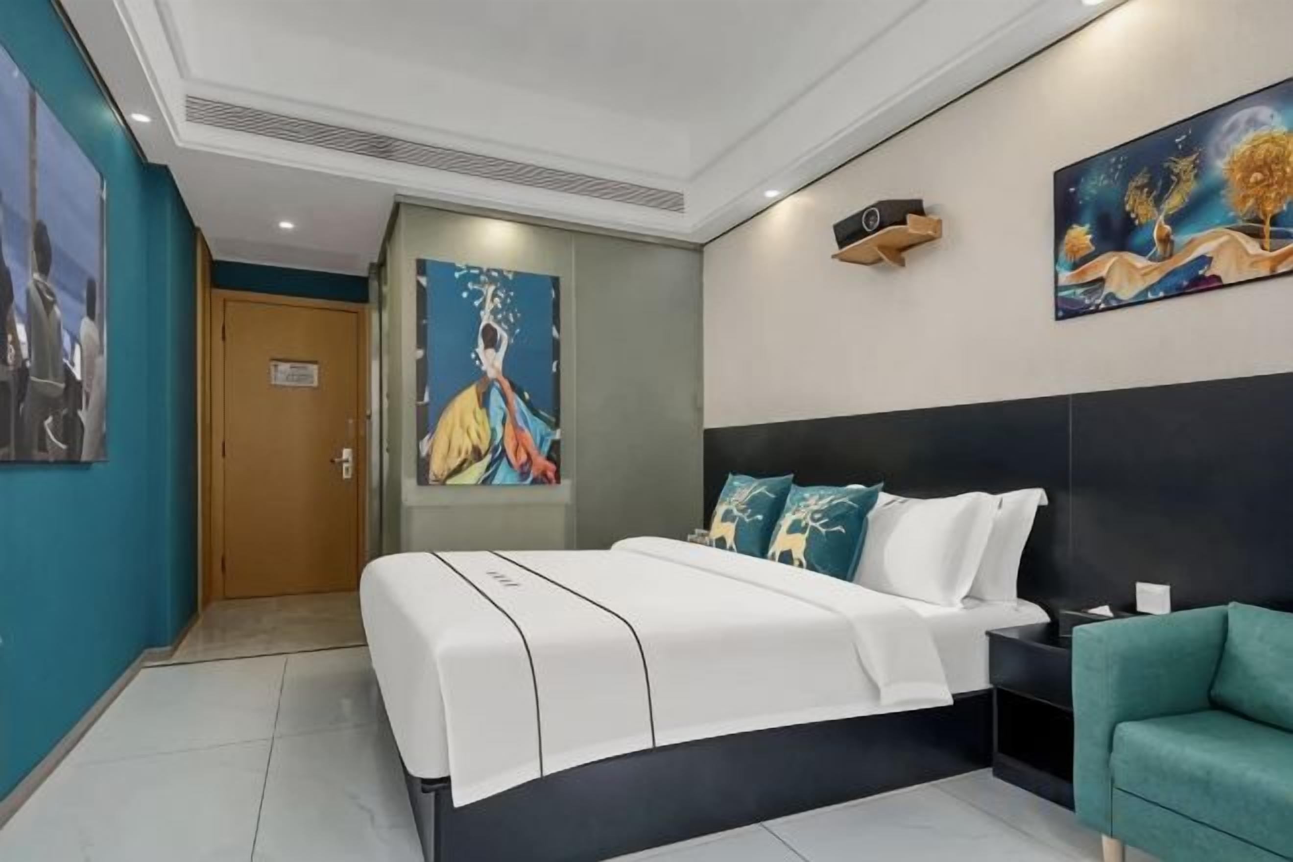 A modern hotel room with a large bed, a desk, and a green armchair.
