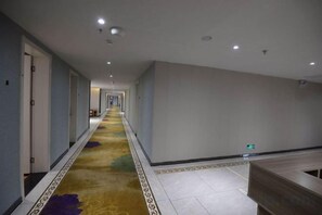 Un pasillo de hotel con piso alfombrado, puertas a la izquierda y un mostrador de recepción a la derecha.