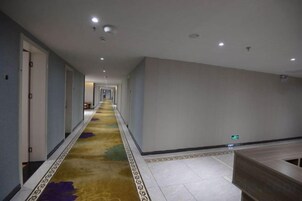 Un pasillo de hotel con piso alfombrado, puertas a la izquierda y un mostrador de recepción a la derecha.