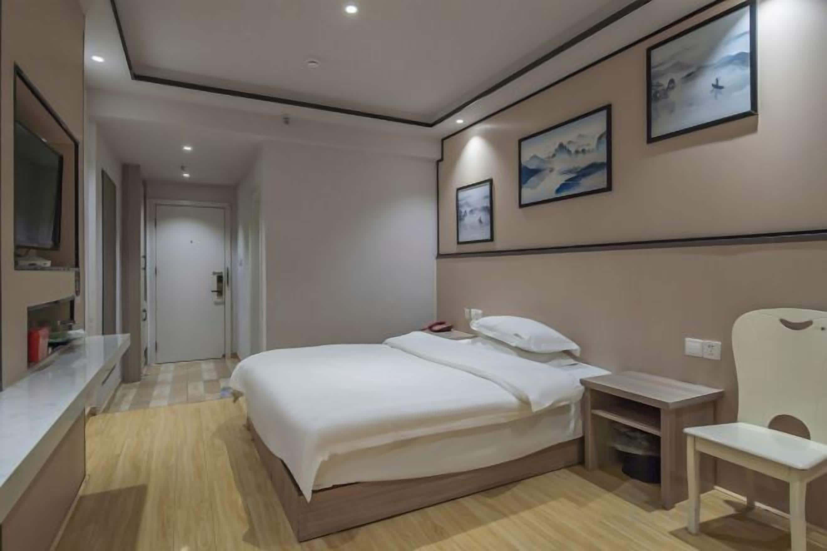 A hotel room with a bed, bedside table, chair, and artwork on the wall.