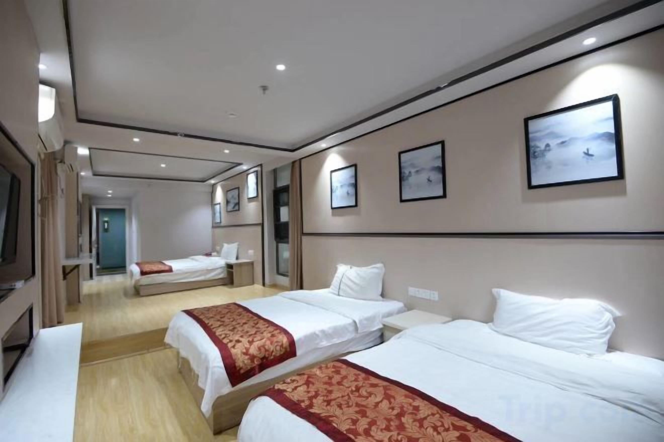 A hotel room with two beds, a television, and a hallway leading to another room.