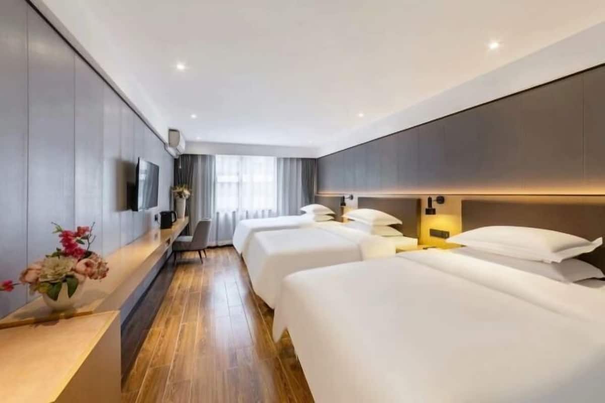 Habitación de hotel con dos camas, un televisor, un escritorio con un florero y una ventana con cortinas.