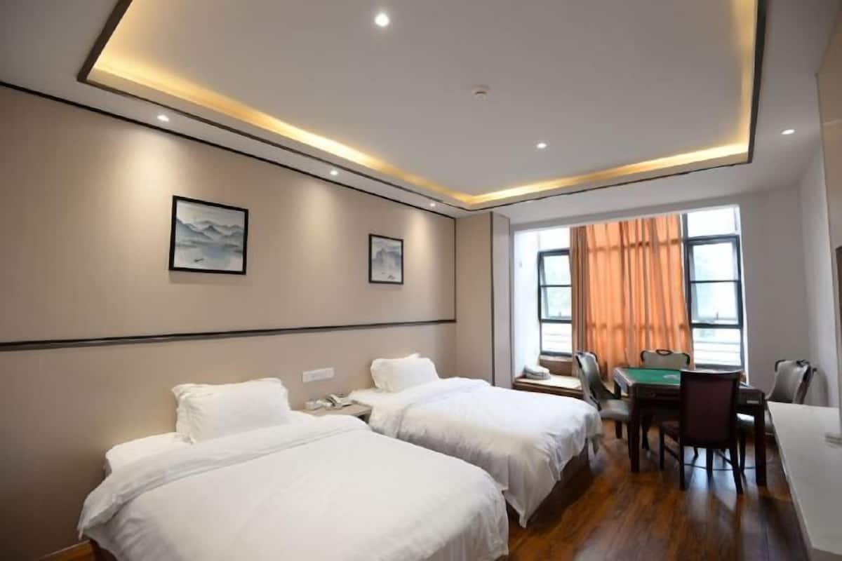 Habitación de hotel con dos camas, un escritorio con sillas, una ventana con cortinas y obras de arte en las paredes.