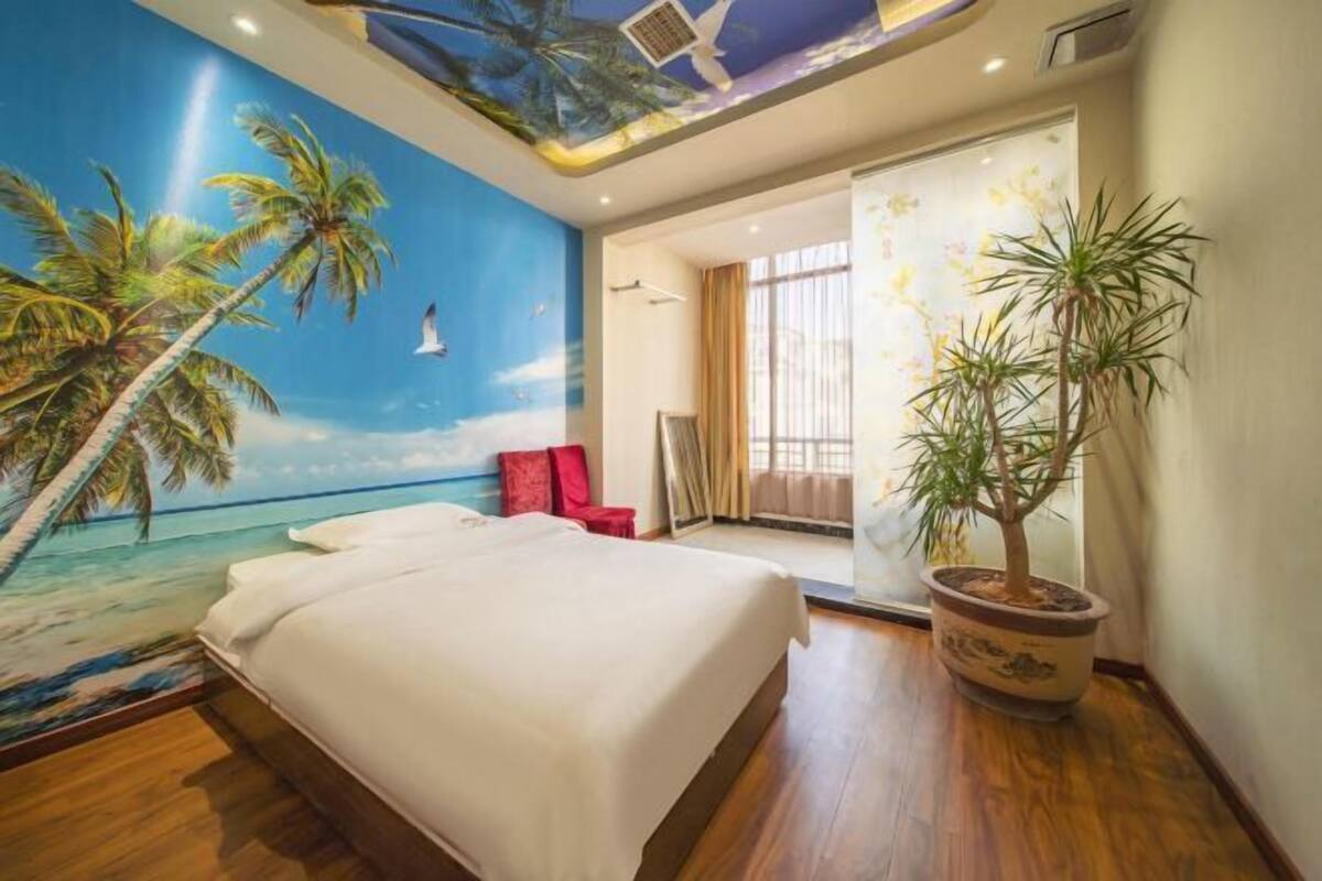 Un dormitorio con un mural de una playa, una cama, una planta en maceta y un patio corredizo que da a un balcón.