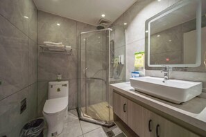 Un baño moderno con ducha de vidrio, inodoro blanco, lavamanos con espejo y un cesto de basura.