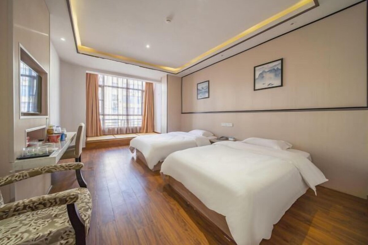 Habitación de hotel con dos camas, un escritorio con silla, una ventana con cortinas y obras de arte en las paredes.