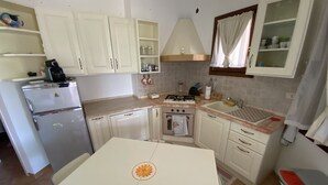 Una cocina compacta con armarios blancos, estufa a gas, refrigerador y una mesa de comedor con un centro decorativo.