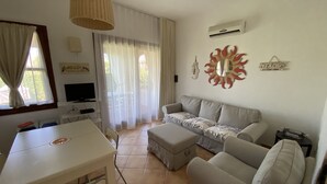 Una sala de estar con un sofá, una mesa de comedor, un televisor y un ventilador de techo.