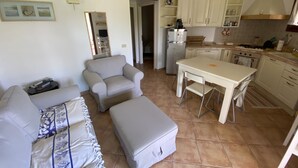 Un espacio habitable compacto con sofá, sillón, otoman, kitchenette y comedor.
