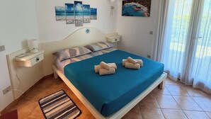 Un dormitorio con cama, mesita de noche, lámpara de pared, un cuadro y ventana con cortinas.