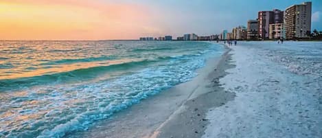 A beach with waves, a clear sky, and buildings in the background.