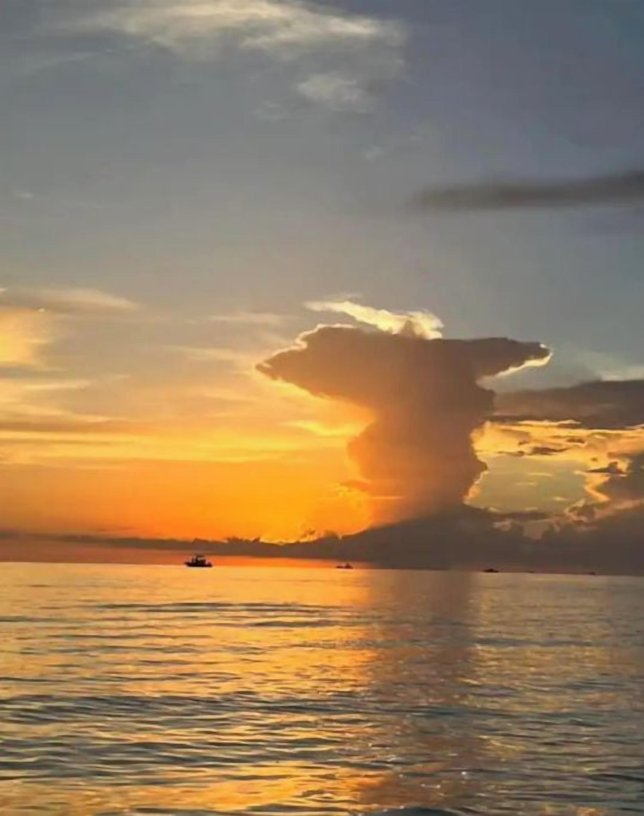 A sunset over a body of water with a prominent cloud formation.