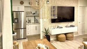 A modern kitchen with stainless steel appliances, a large flat-screen TV mounted on the wall, and two woven pendant lights.