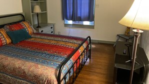 A bedroom with a bed, bedside table, lamp, and a window with curtains. - Boho Hip Bungalow (Bisbee)