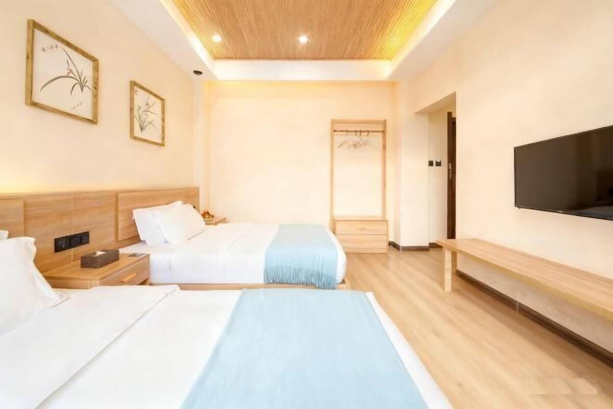 A hotel room with two beds, a TV, a wooden bench, and a wardrobe.