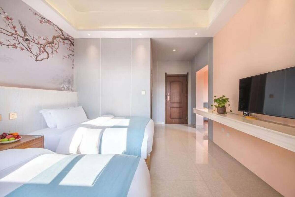 A hotel room with two beds, a TV, a plant, and a wall with a floral mural.