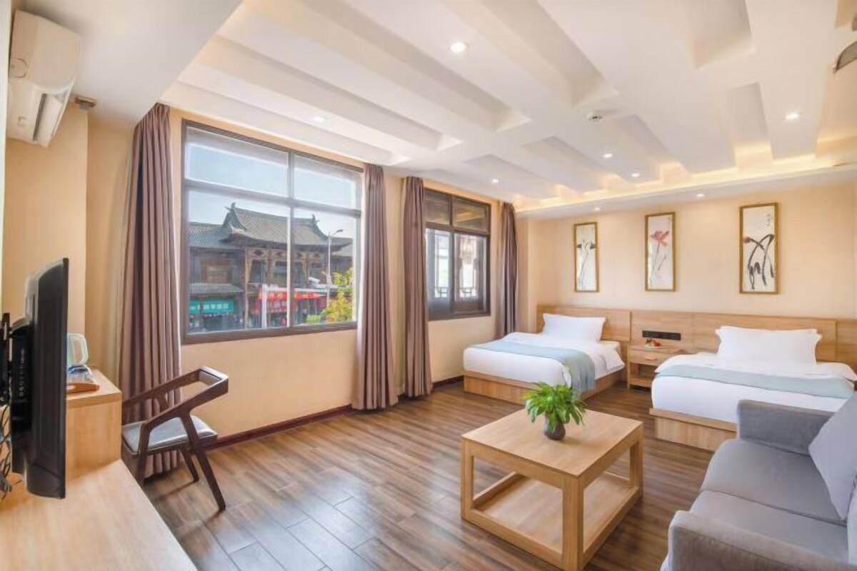 A hotel room with a large window, a bed, a sofa, a TV, and a coffee table.