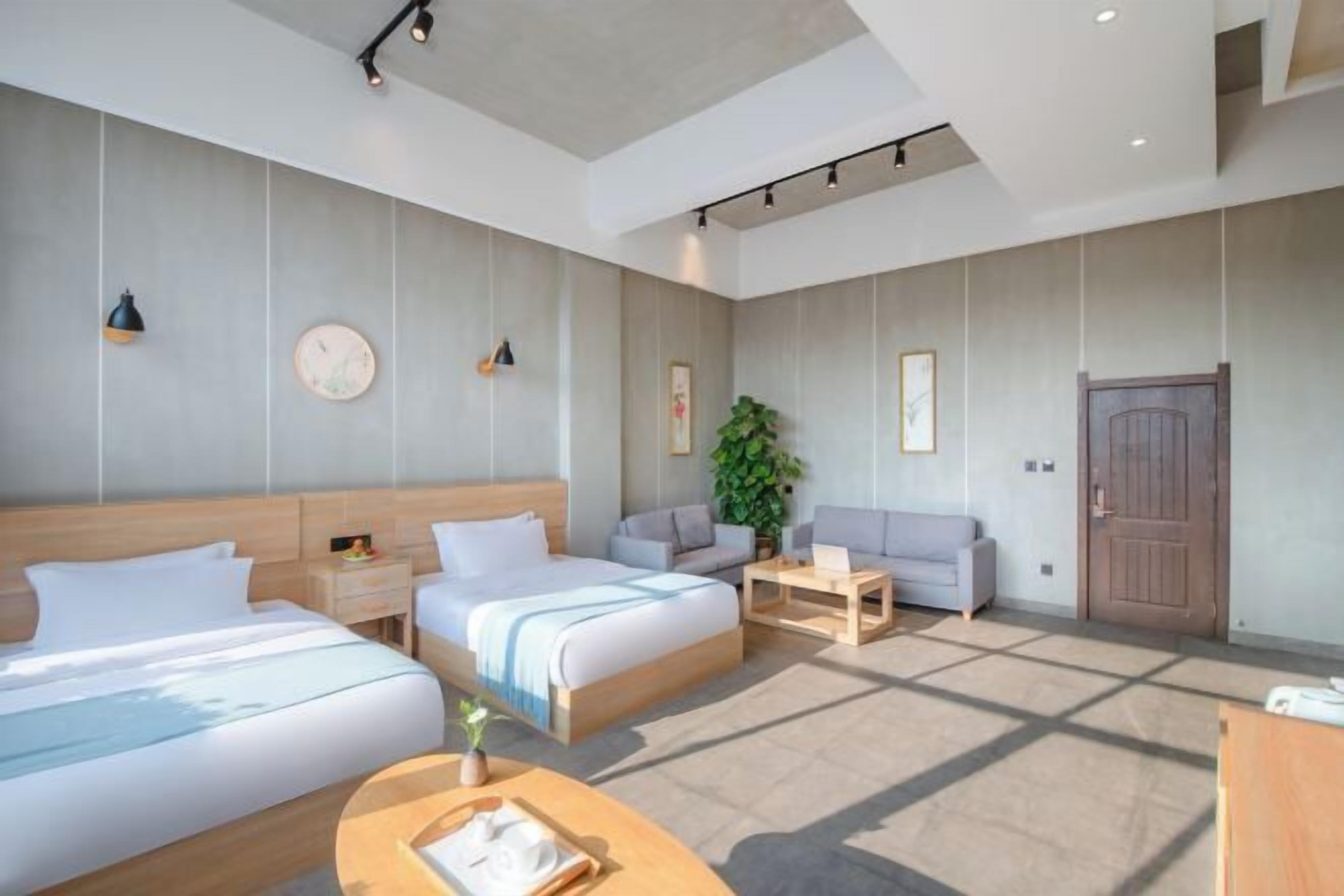 Quarto de hotel moderno com duas camas, um sofá, uma mesinha e uma janela grande.