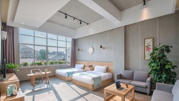 A modern hotel room with two single beds, a sofa, a coffee table, and a large window offering a view of the cityscape. - Yanchaoyang Boutique Inn (Jianshui)