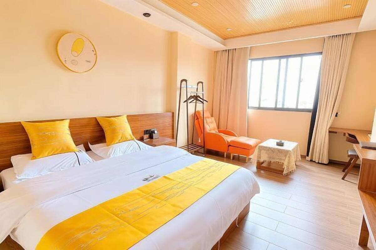 A hotel room with a large bed, a desk, a chair, a small table, a coat rack, and a window with curtains.