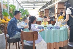 An outdoor dining area with tables covered in tablecloths, surrounded by plants and wooden structures.