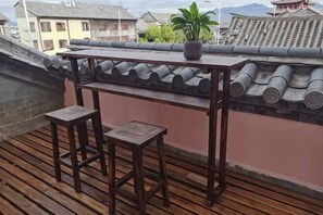Una mesa de madera con dos taburetes en un balcón con techo de tejas tradicionales.