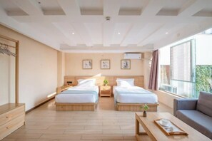 Quarto de hotel moderno com duas camas, um sofá, uma mesa de madeira e uma janela grande.