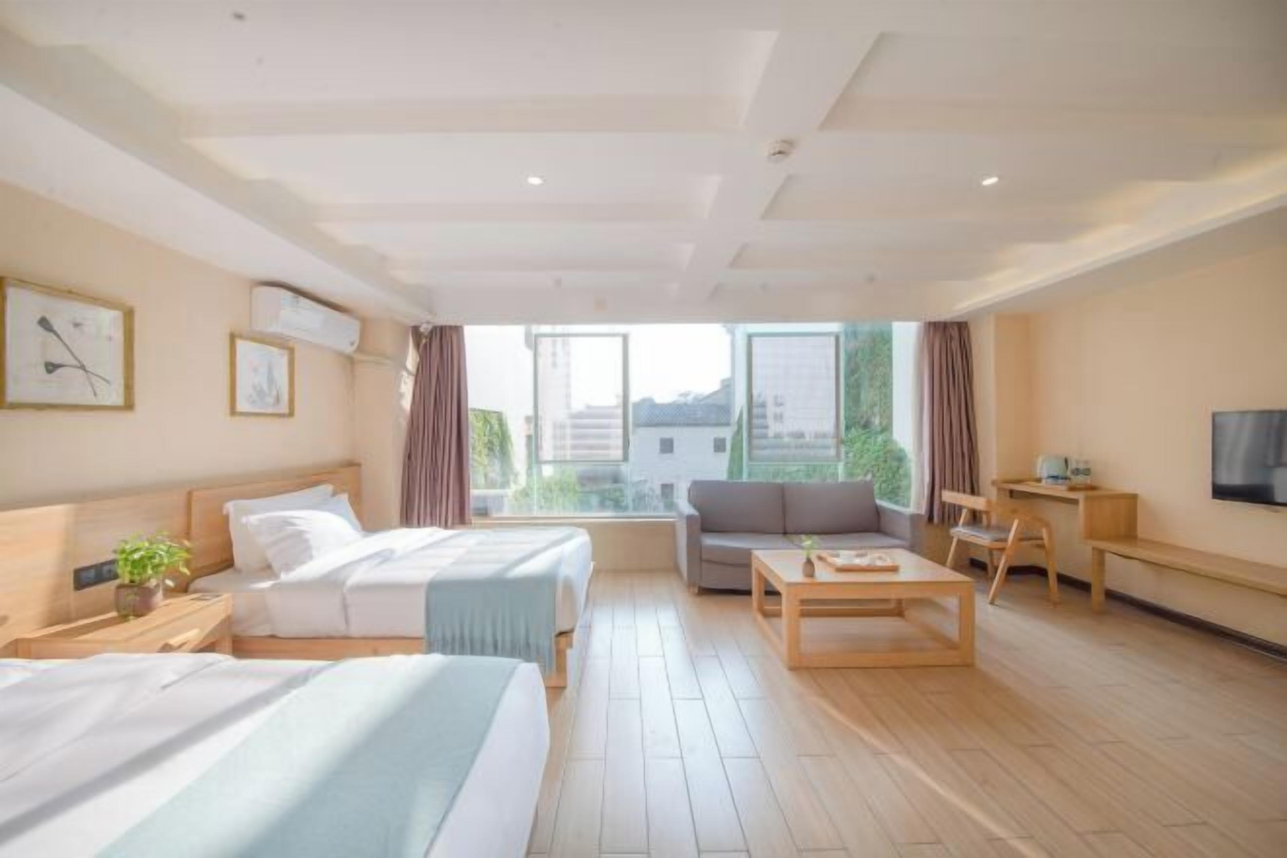 Habitación de hotel con dos camas, un sofá, una mesa de centro, un televisor y ventanas amplias.