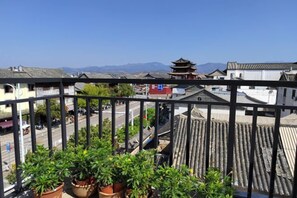 A balcony with potted plants, traditional buildings, and a clear sky.