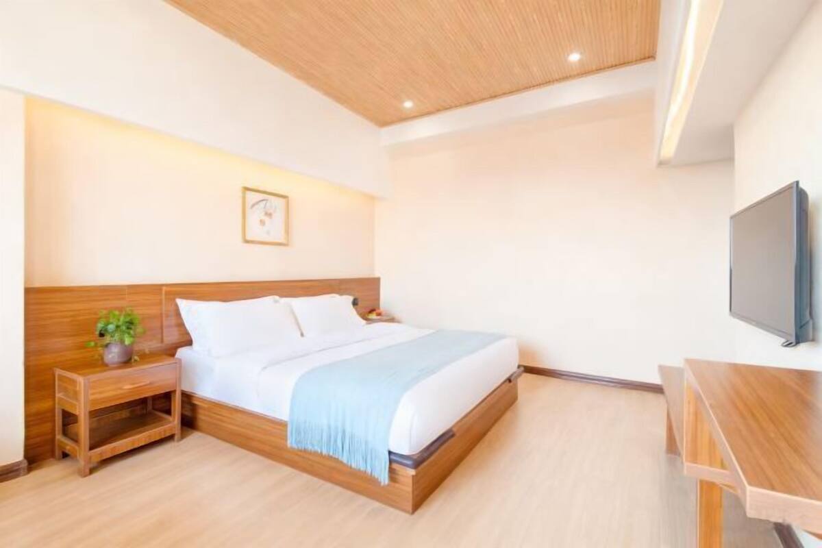 A modern hotel room with a wooden bed, bedside table, and a TV.