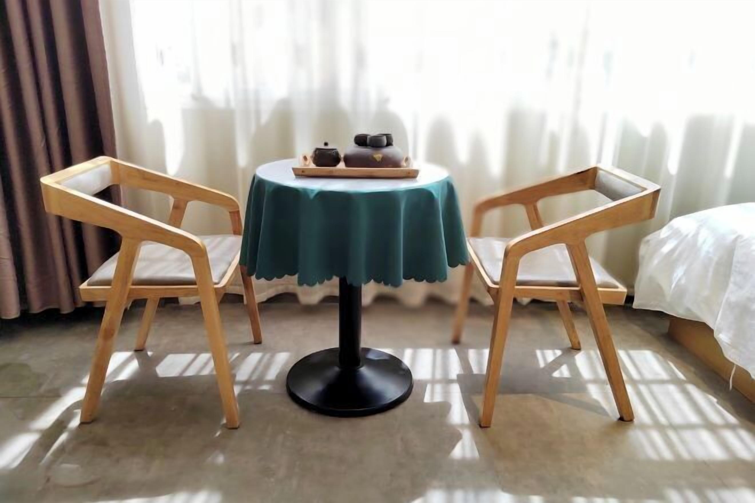 A small round table with a teal tablecloth, two wooden chairs, and a tray with a teapot and cups.
