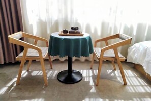 Uma mesa redonda pequena com toalha de mesa verde-água, duas cadeiras de madeira e uma bandeja com bule e xícaras.