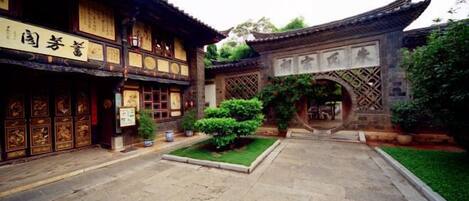 A traditional courtyard with a tiled floor, a wooden gate, and a building with detailed woodwork and signage.