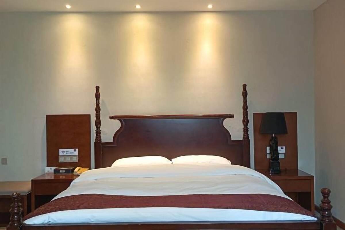 Una cama con dosel, un cabecero de madera, dos mesitas de noche y una mesita con una lámpara.