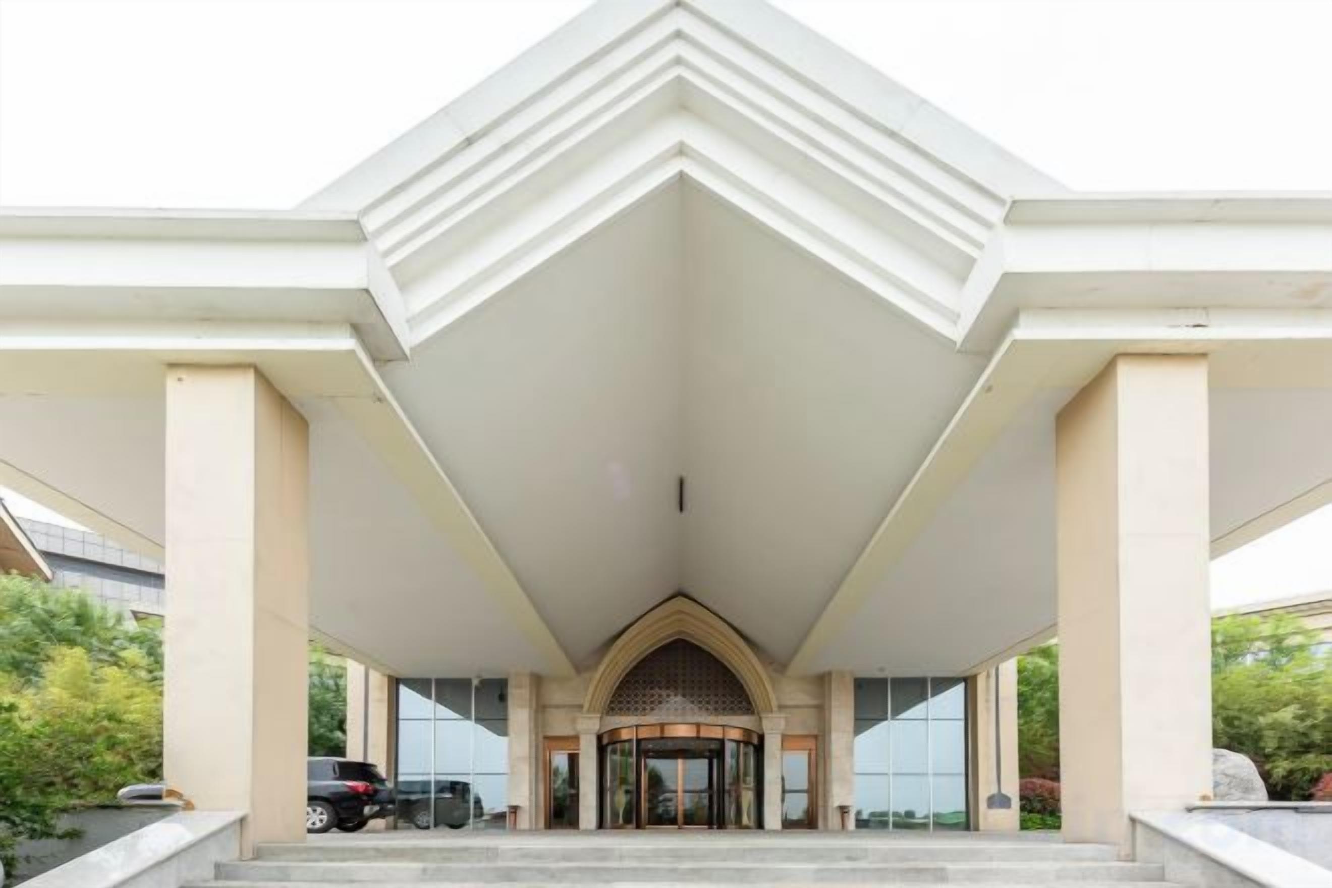 A hotel entrance with a central archway, a covered walkway, and a car parking area.