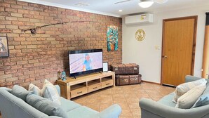 Un salon avec un mur en briques, un téléviseur, deux canapés, un meuble en bois et une porte.