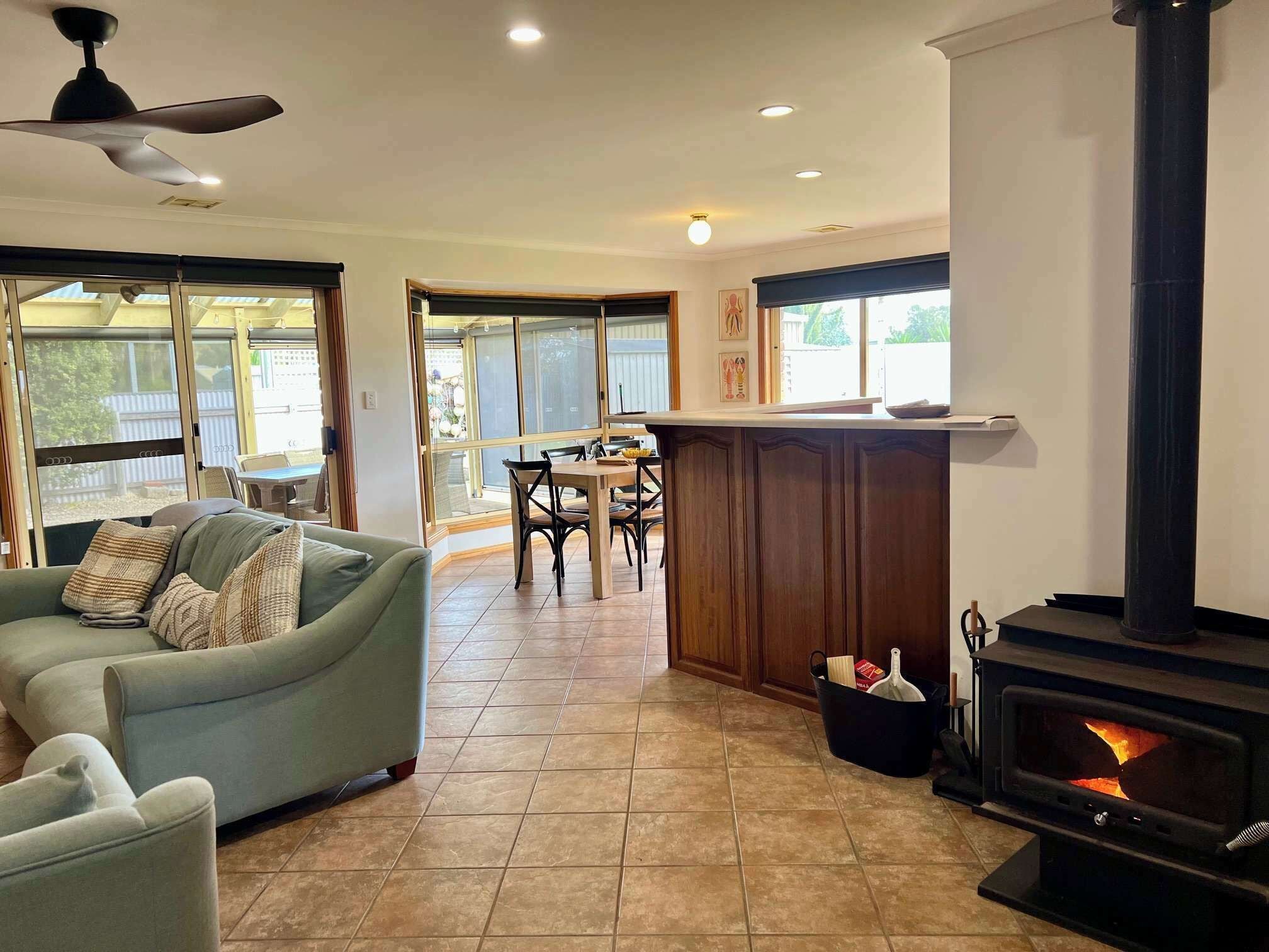 A living room with a sofa, a dining table with chairs, a fireplace, and a ceiling fan.