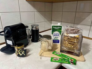 A kitchen counter with a coffee maker, a milk carton, a jar of sugar, a box of cereal, and a bag of nuts.