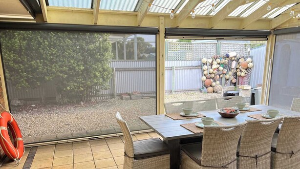 Une terrasse couverte avec une table dressée pour le repas, des chaises en osier et un anneau de sauvetage.