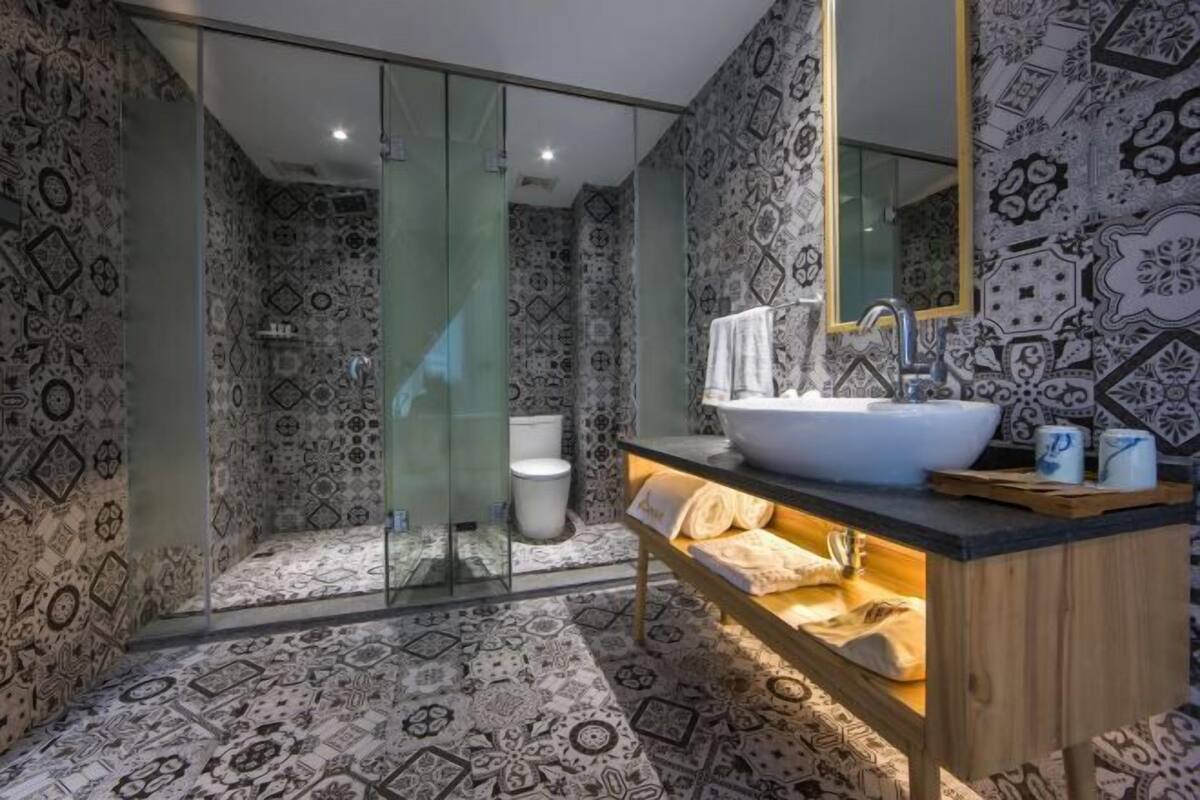 Un baño con baldosas estampadas, cabina de ducha de cristal, lavabo con espejo y perchero.