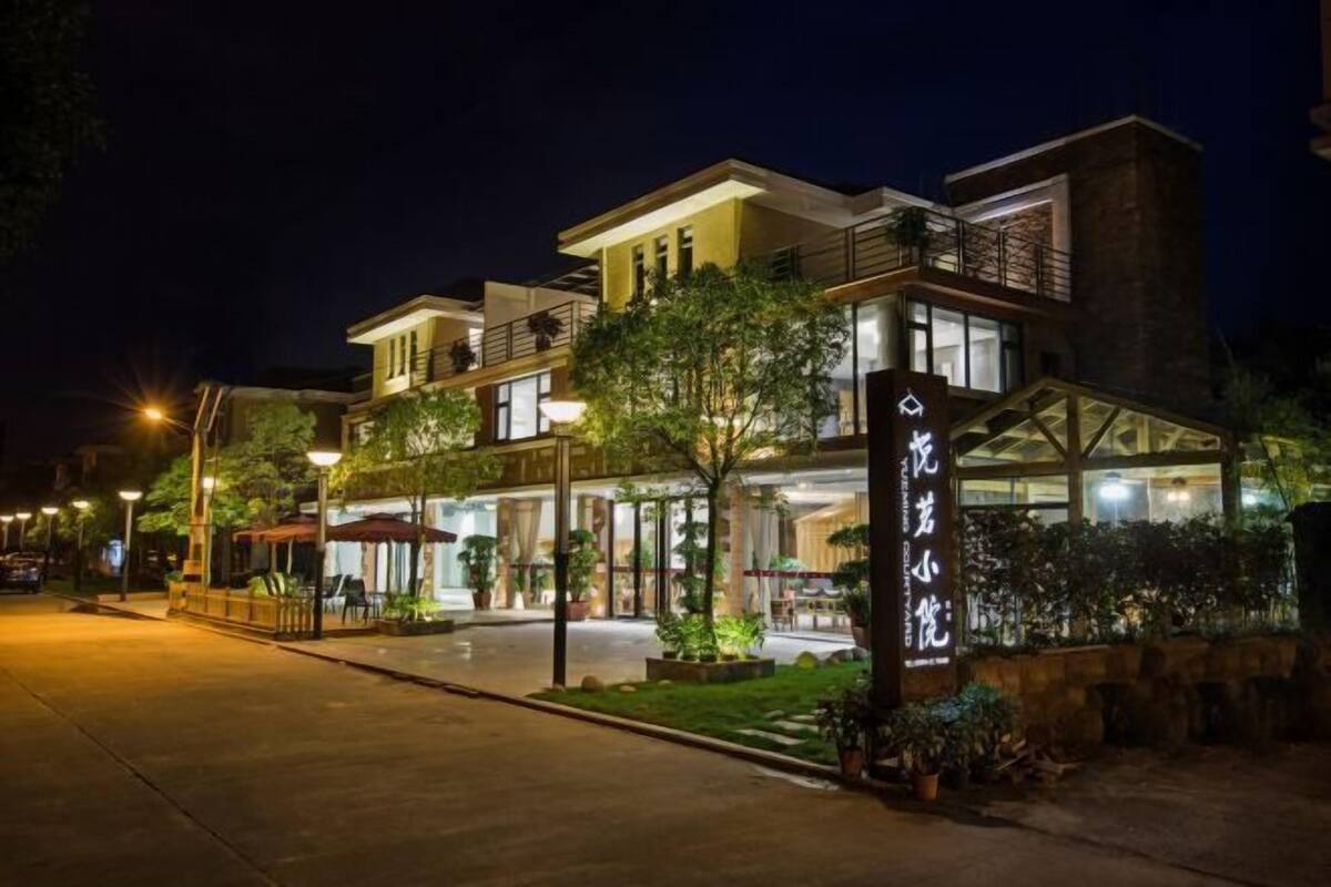 Un hotel moderno con una entrada bien iluminada, un área de estar al aire libre y un cartel.