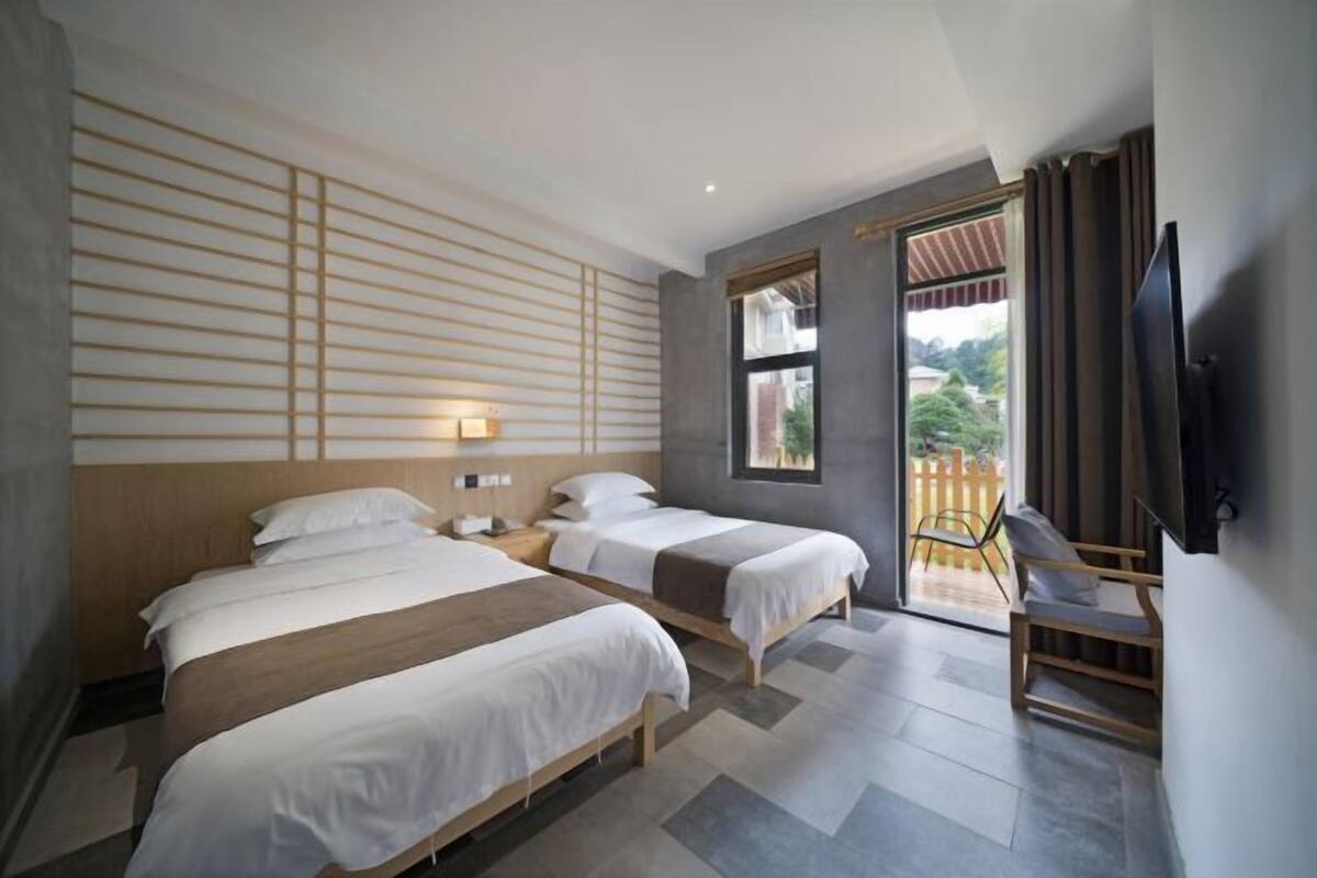 Habitación de hotel con dos camas, televisión, escritorio y vista al exterior.