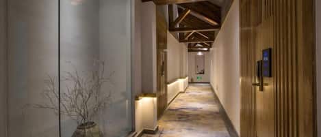 A hallway with a patterned carpet, a vase with branches, and a wooden door with a lock.